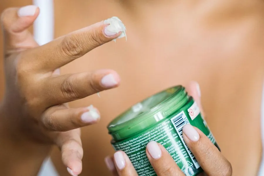 A hand dipping into a skin cream pot.
